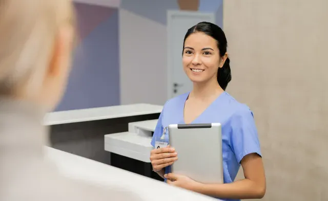 Medical assistant at front desk holding tablet smiling with patient